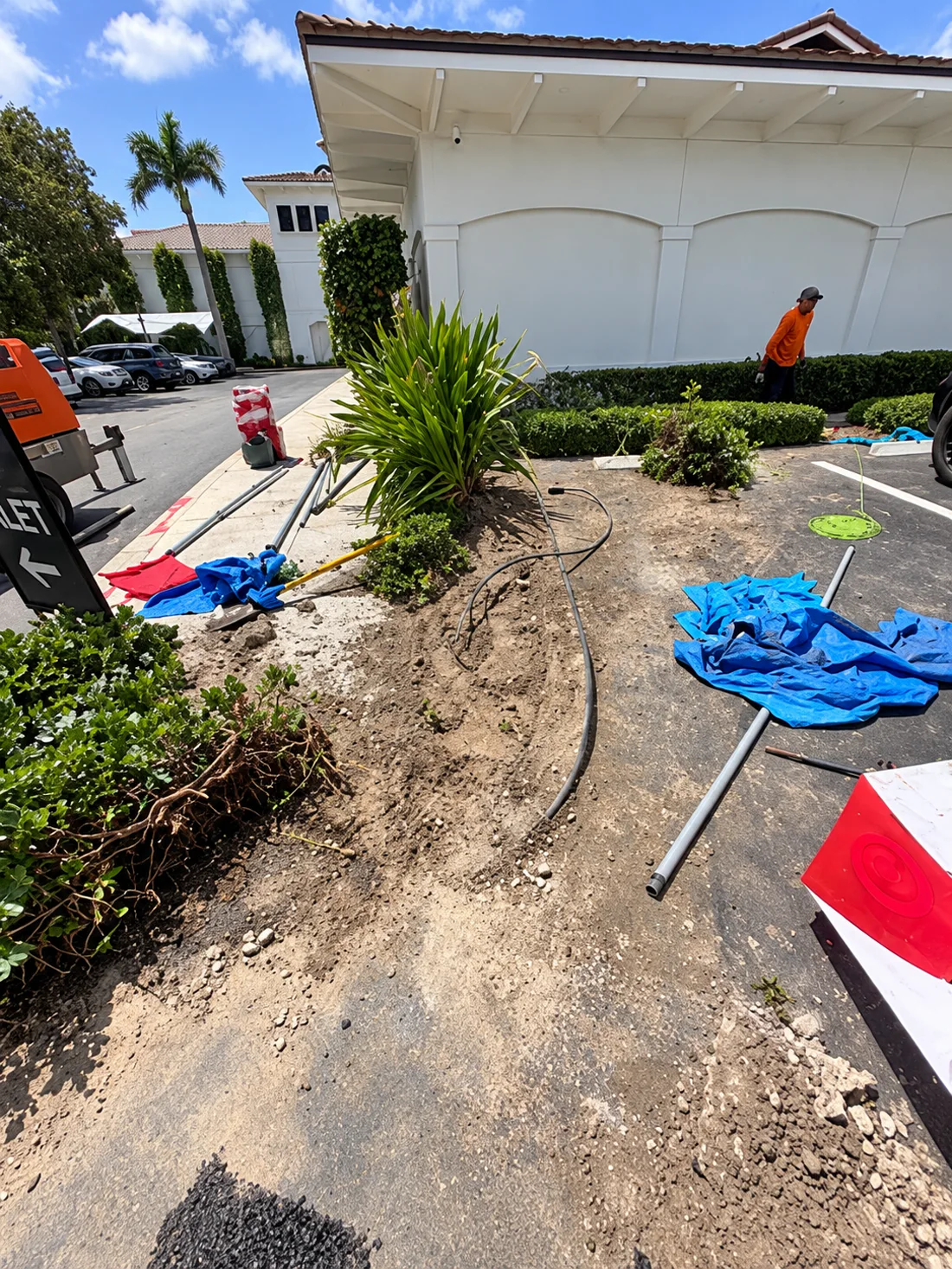 FBR work underway beside a landscaped property, with conduit and tools at the excavation